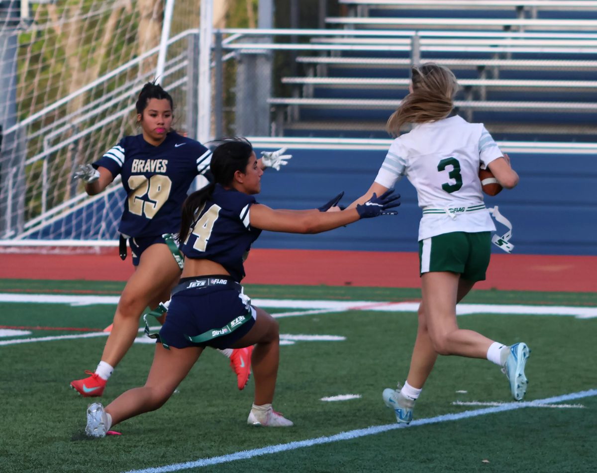 Jada Orsini and Coco Moramarco closing in on an opposing player with the ball, attempting to pull her flag.